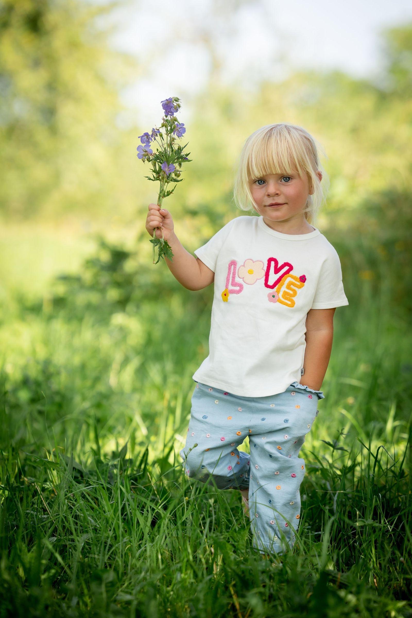 Kind steht im Gras und hält einen kleinen Blumenstrauß in der Hand | A child is standing in the grass, holding a small bouquet of flowers